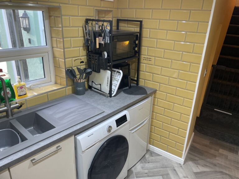 Kitchen with yellow tiles, a sink, washing machine and microwave.