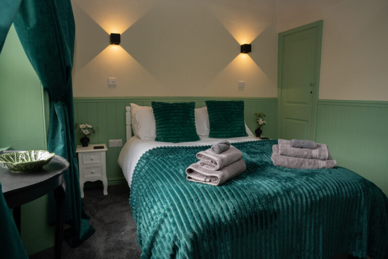 Double bedroom with a teal bed and folded towels against green panelling.