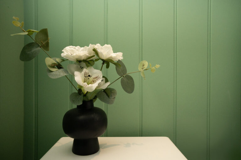 White roses in a black vase against green bedroom panelling.