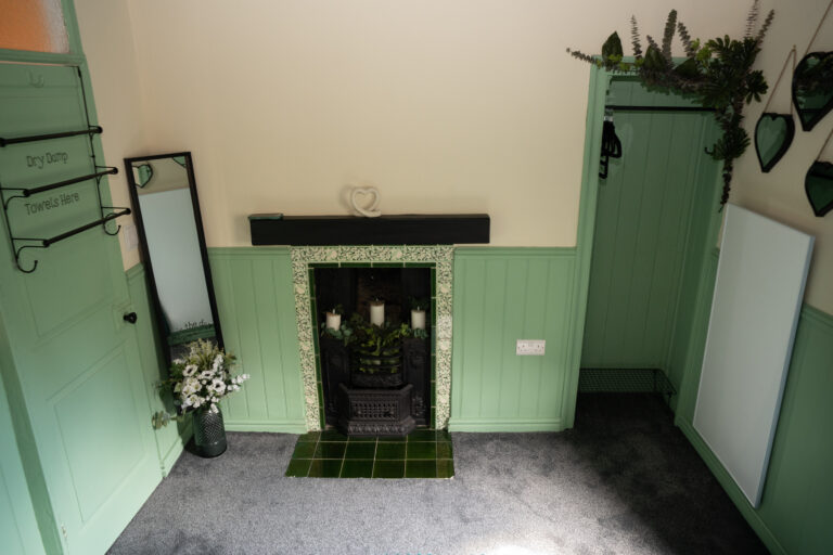 Green panelled bedroom with a cast iron fireplace and a tall mirror.