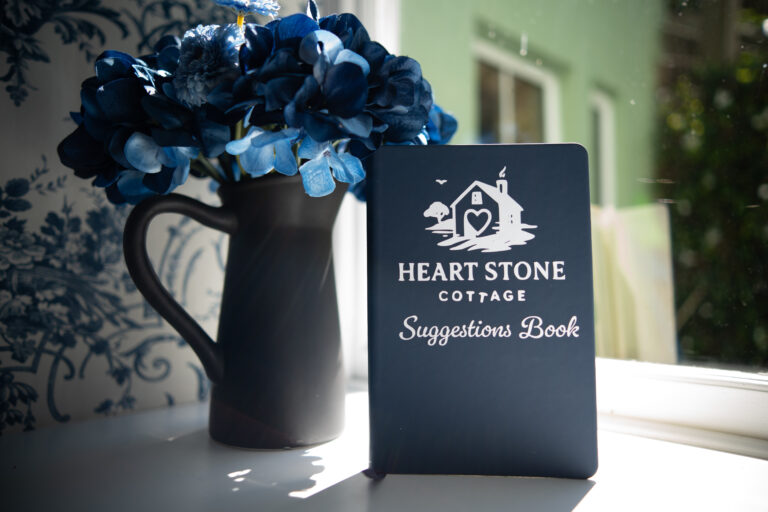 The Heart Stone Cottage suggestions book on a windowsill beside blue hydrangeas.