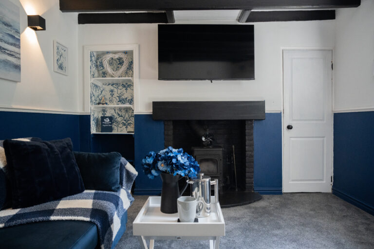 Navy living room with a cast iron log burner and a jug of blue hydrangeas.