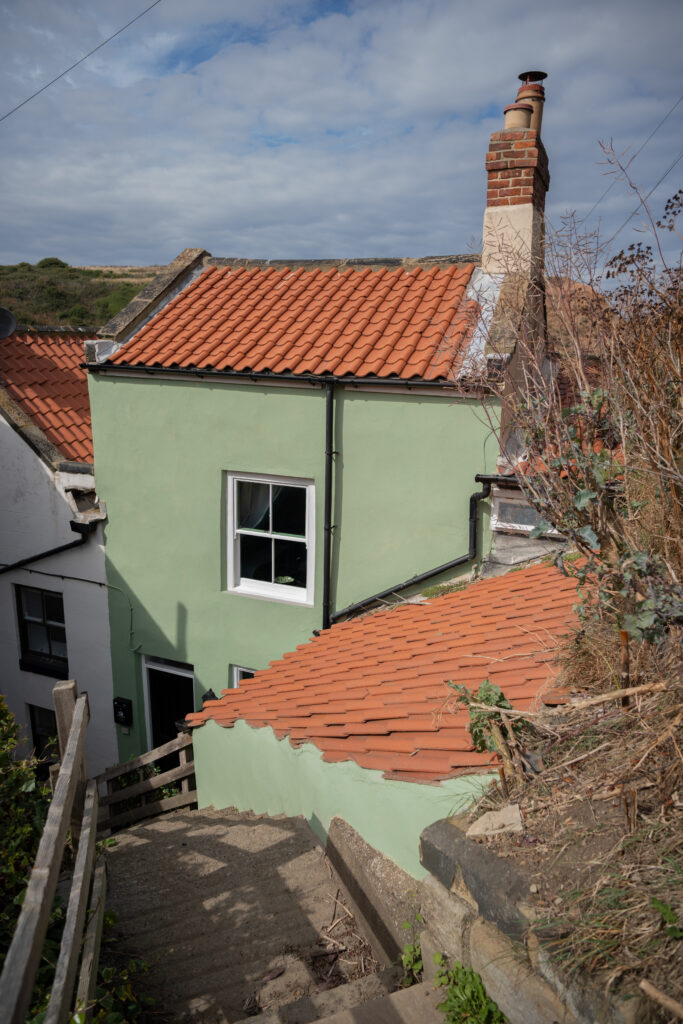 The green-painted exterior of Heart Stone Cottage among the pantile roofs of Staithes.