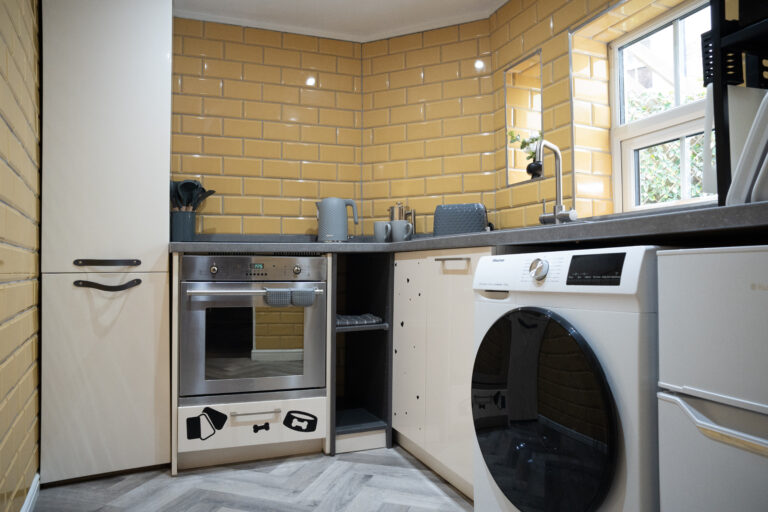Kitchen with oven, washing machine and yellow metro tiles.